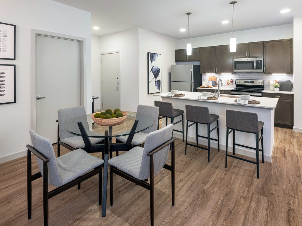 A modern kitchen with a glass dining table and grey chairs.
