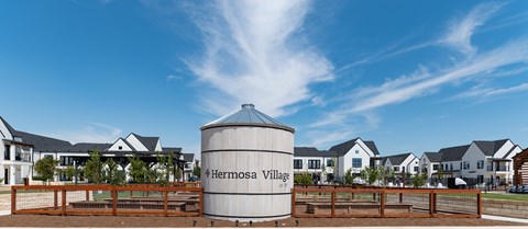 A large silo with the words Hermosa Village on it in front of a row of houses.