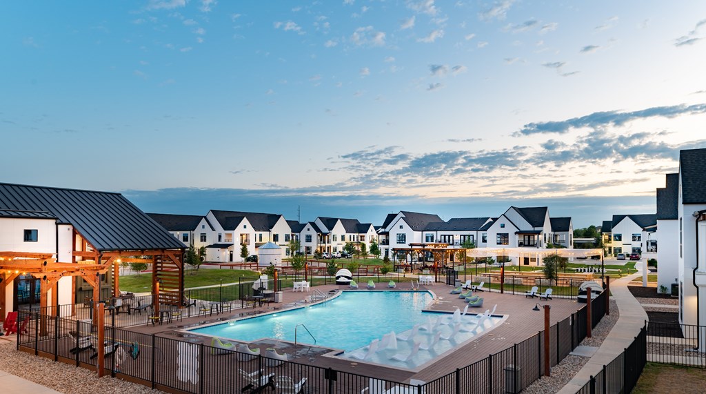 A large outdoor swimming pool surrounded by a fence and a wooden pergola.
