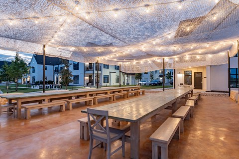 A large outdoor dining area with wooden tables and benches under a canopy of string lights.