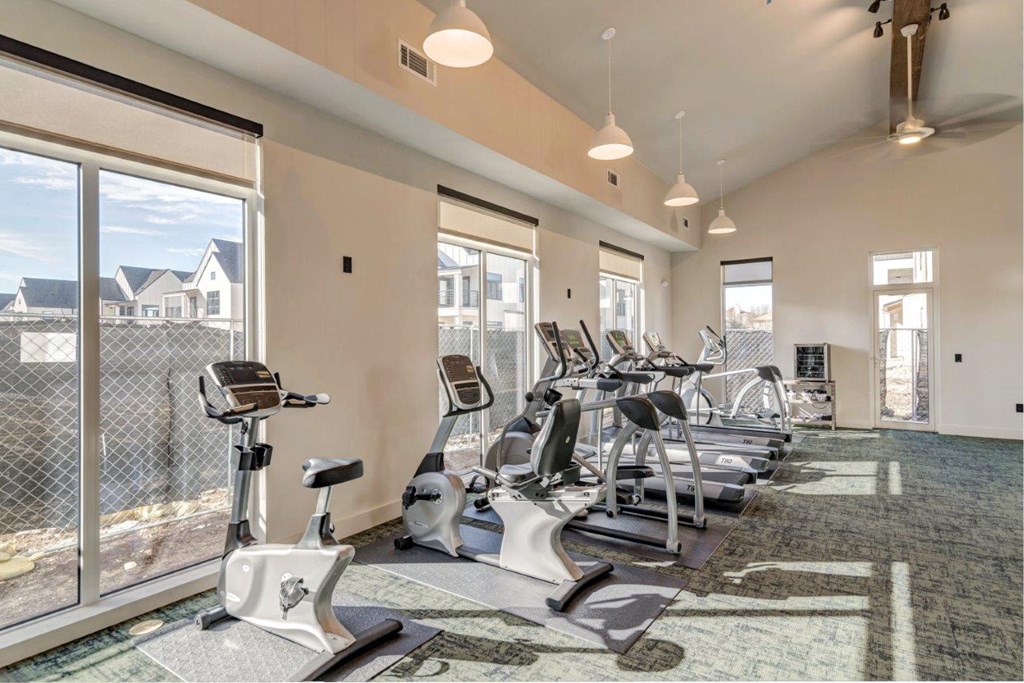 a gym with cardio machines and windows at the district flats apartments in lenexa