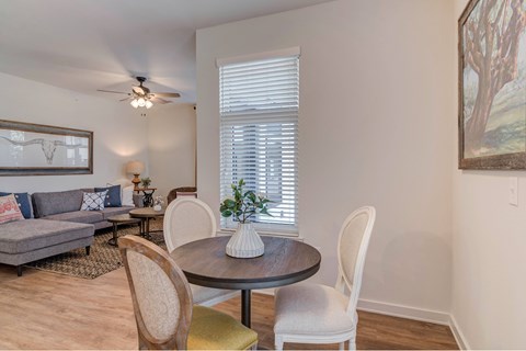 A living room with a grey sofa, a round table with four chairs, and a painting on the wall.