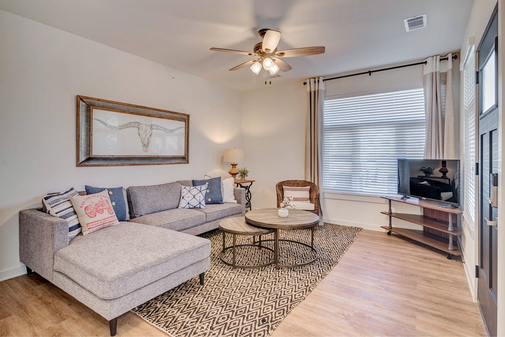 A living room with a grey couch, a round coffee table, and a ceiling fan.