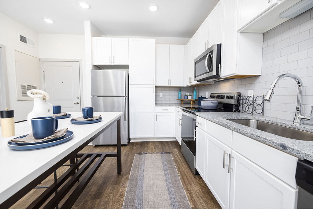 A modern kitchen with white cabinets and a wooden floor.