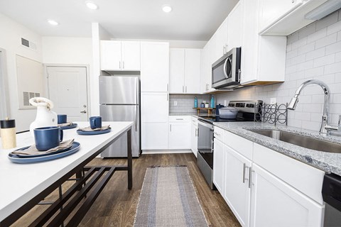 A modern kitchen with white cabinets and a wooden floor.