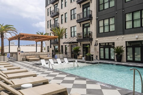 A pool with sun loungers and a building in the background.