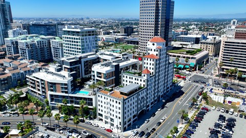 A cityscape with a mix of modern and older buildings, a clear sky, and a busy intersection with cars.