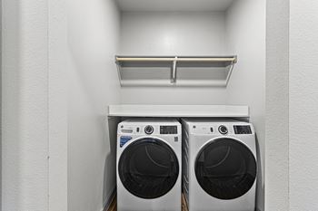 a washer and dryer in a laundry room with white walls and a shelf