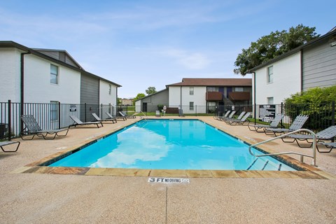 A swimming pool surrounded by chairs and apartment buildings.