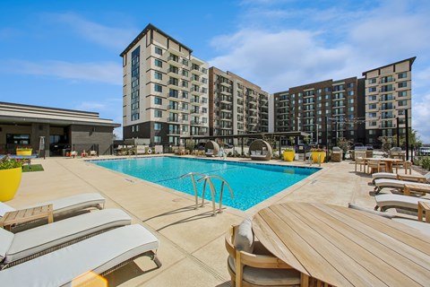 A large swimming pool with sun loungers and a hotel in the background.