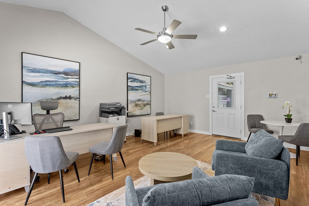 A room with a desk, chairs, and a ceiling fan.