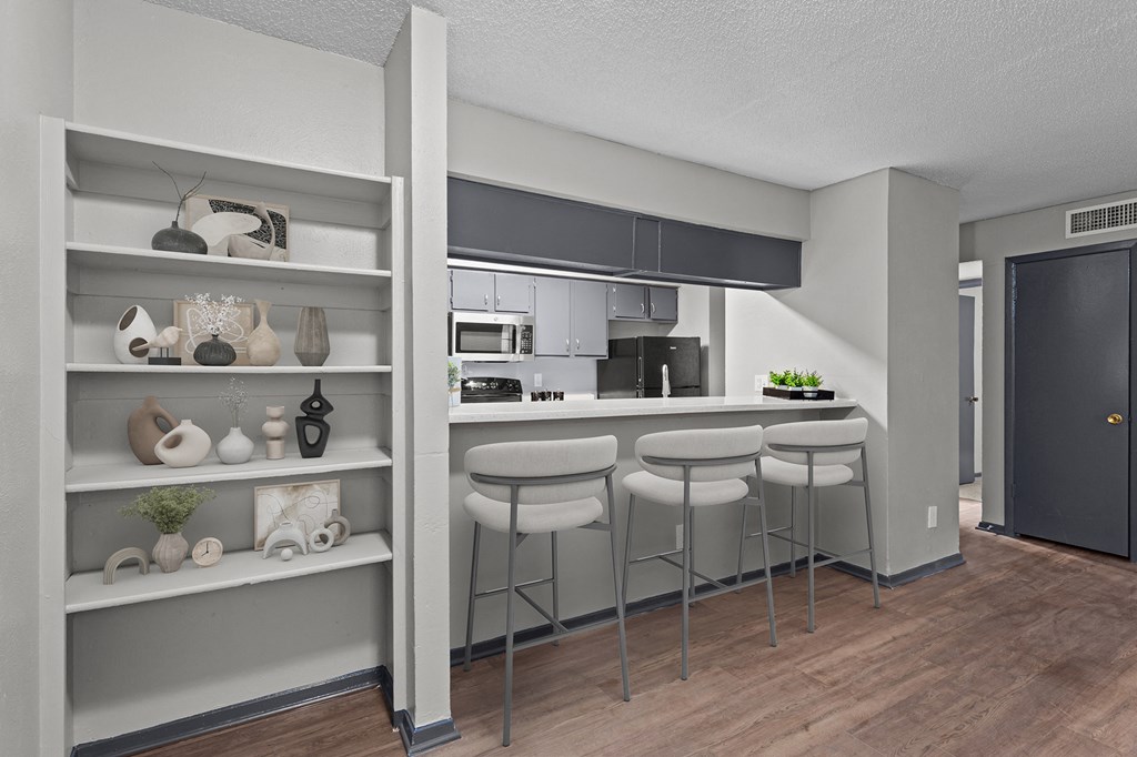 A kitchen with a bar stool and a shelf with decorative items.