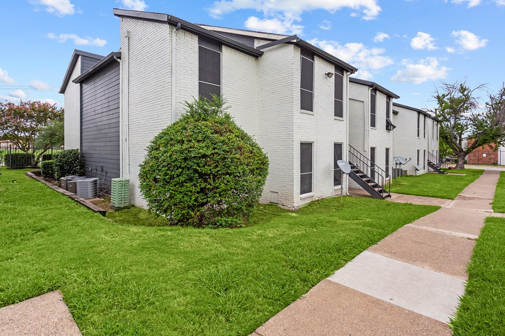 A white building with a green bush in front of it.