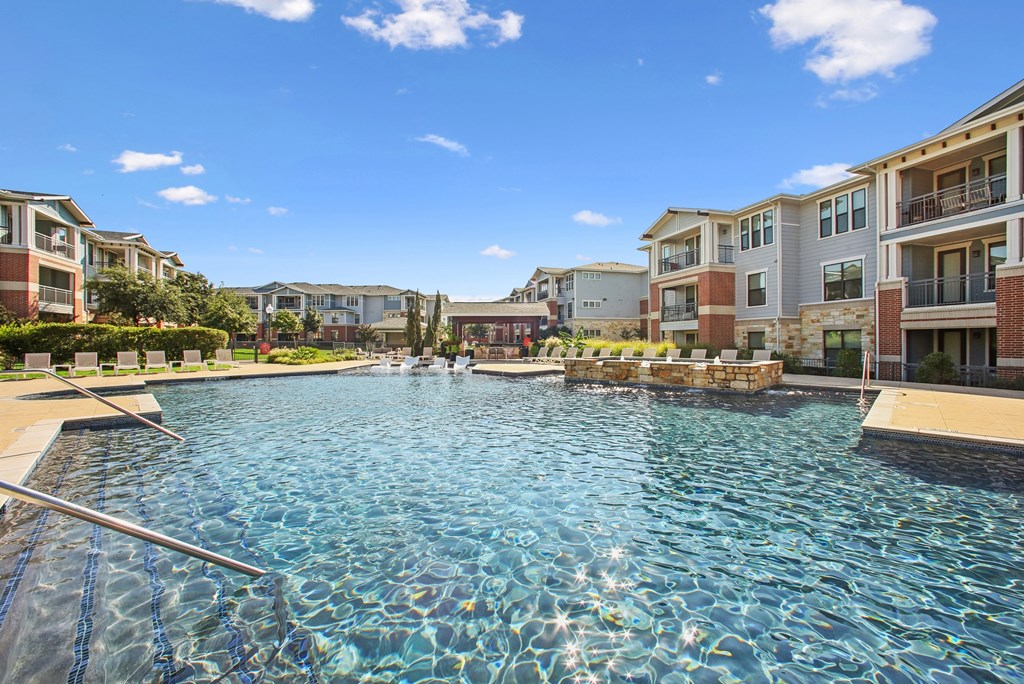 A swimming pool in front of apartment buildings on a sunny day.