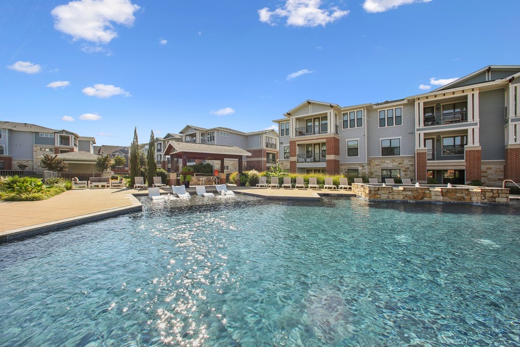A swimming pool in front of apartment buildings on a sunny day.