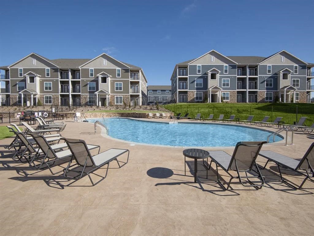an outdoor pool with chairs and chairs around it and an apartment building in the background