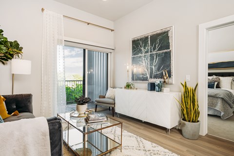 A modern living room with a white couch, a glass coffee table, and a large window with white curtains.