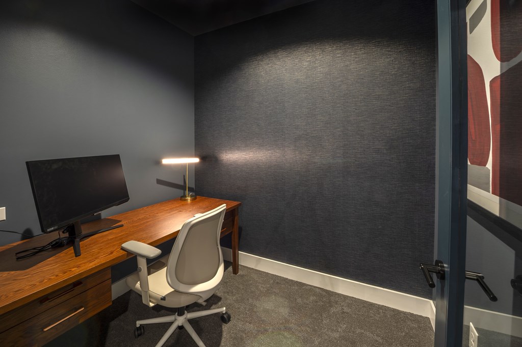 A modern office chair sits in front of a desk with a computer monitor and lamp.
