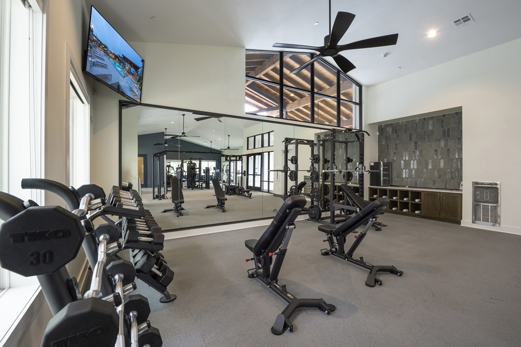 A gym with a row of black weight machines and a flat screen TV mounted on the wall.