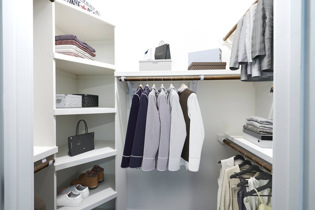 A white closet with clothes hanging and shoes on shelves.