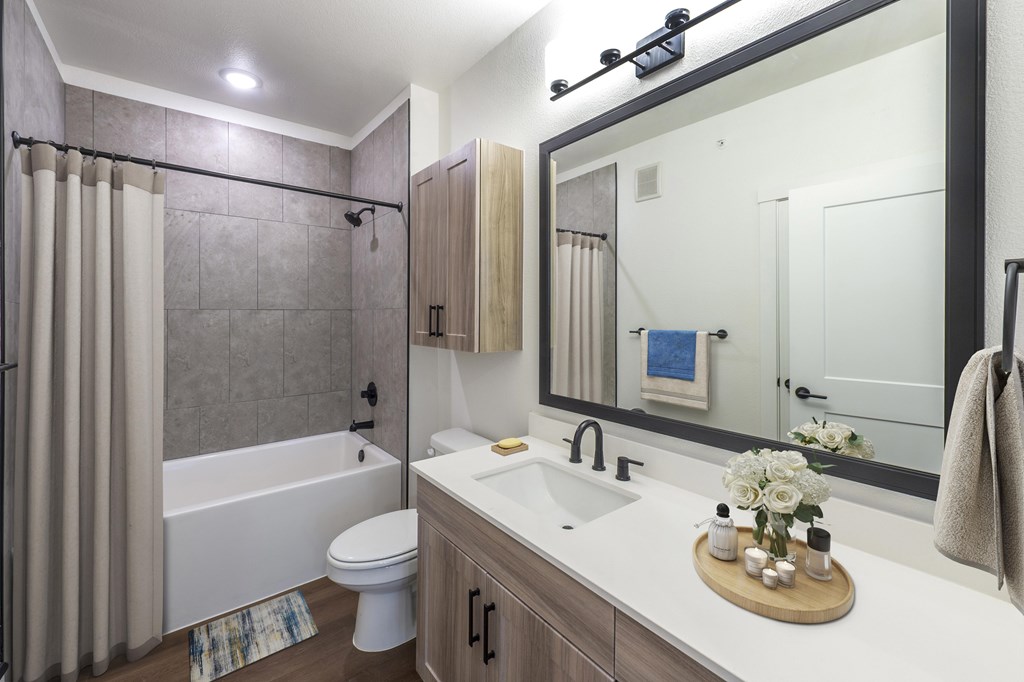 A bathroom with a white tub and sink, a mirror, and a toilet.