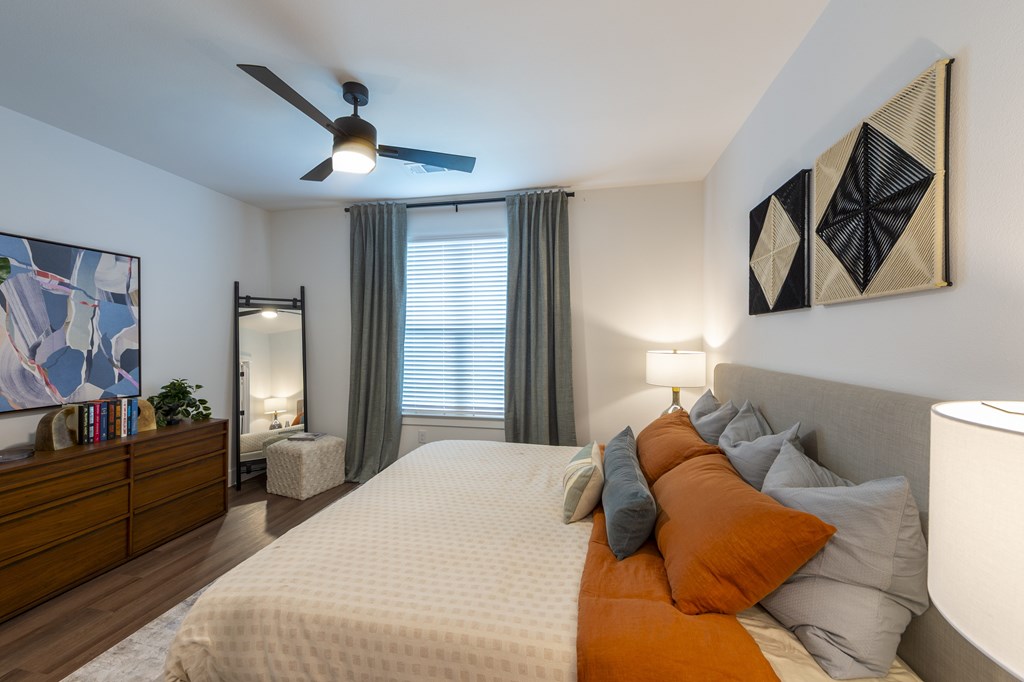 A bedroom with a large bed, a ceiling fan, and a painting on the wall.