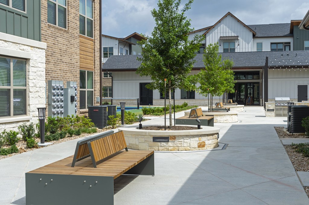 A park area with benches and a tree in front of a building.
