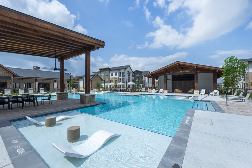 A large outdoor swimming pool with a wooden roof and lounge chairs.
