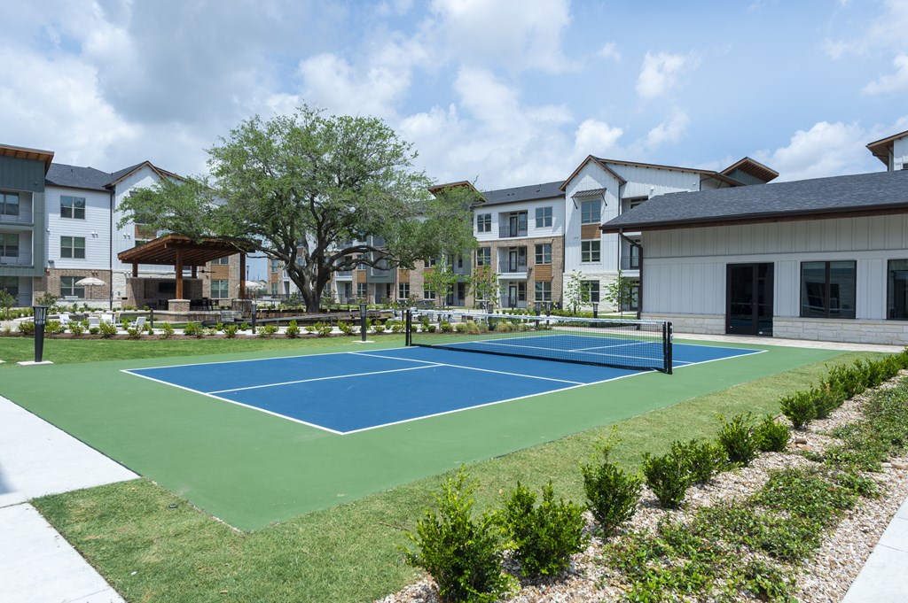 A tennis court is surrounded by bushes and trees.