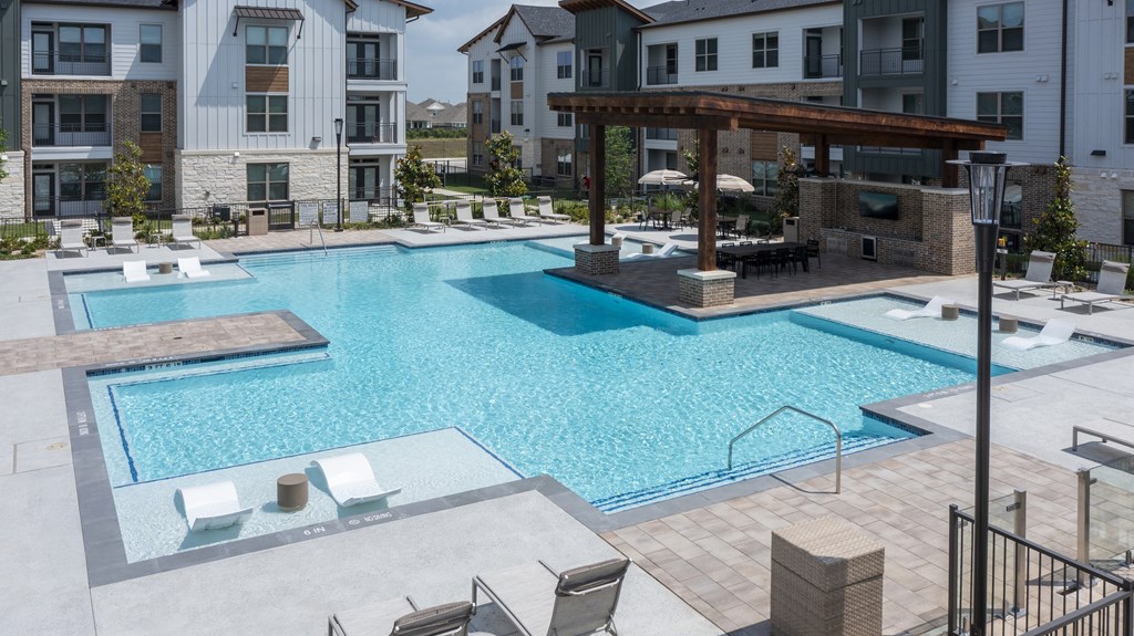 A large outdoor swimming pool with a wooden pergola and lounge chairs.