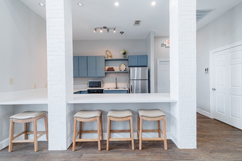 A kitchen with white walls and a white counter top with three stools.