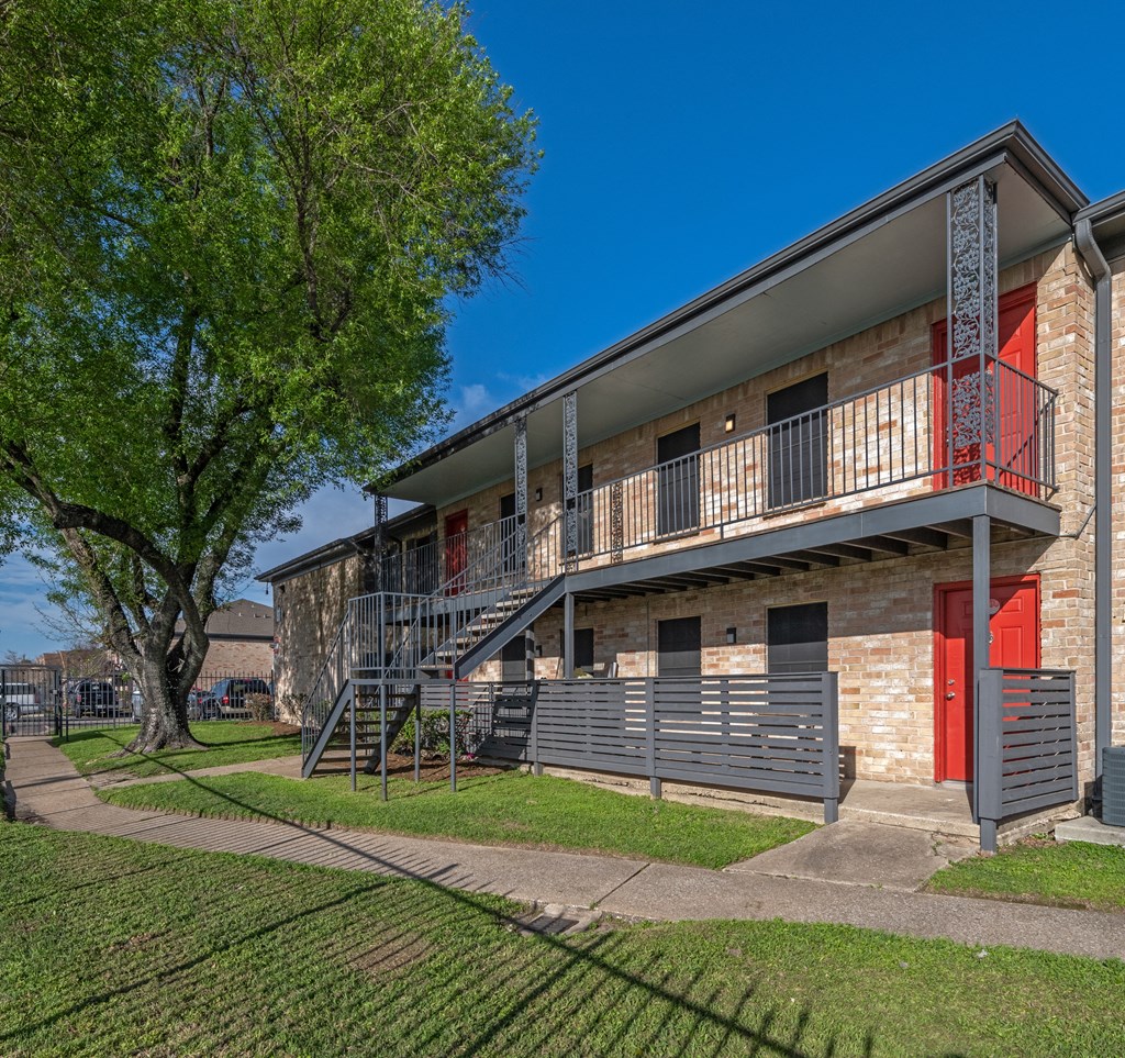 An exterior photo of a two-story apartment building, Costa Mesa Apartments, with stairs and greenery space