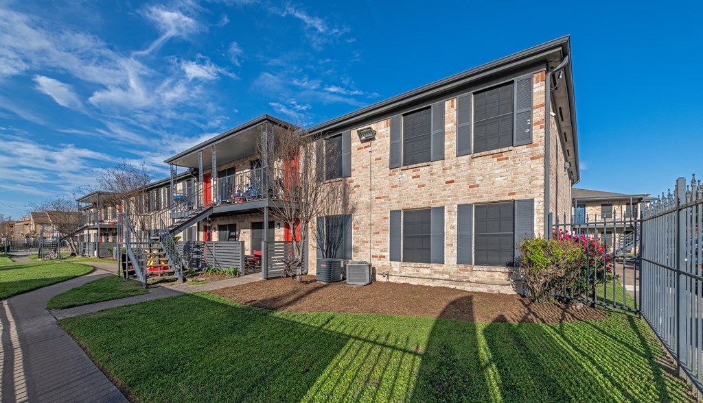 An exterior photo of a two-story apartment  building (Costa Mesa Apartments) with stairs and greenery space