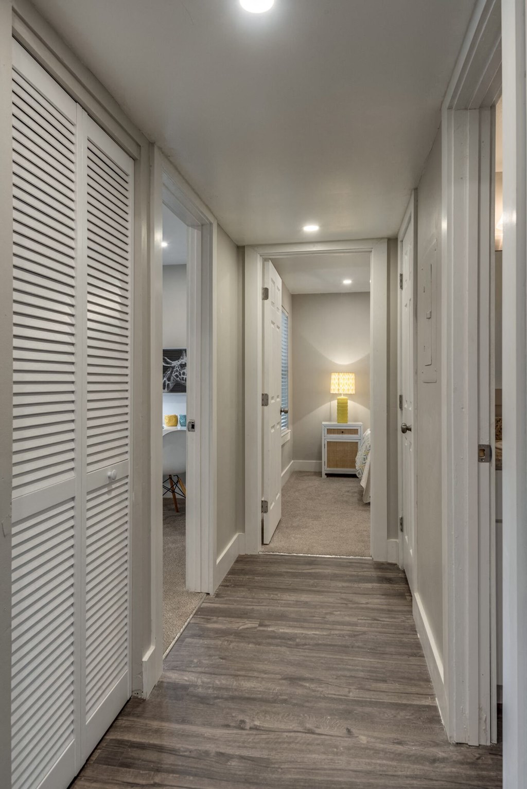 a long hallway with white doors and a bedroom in the end