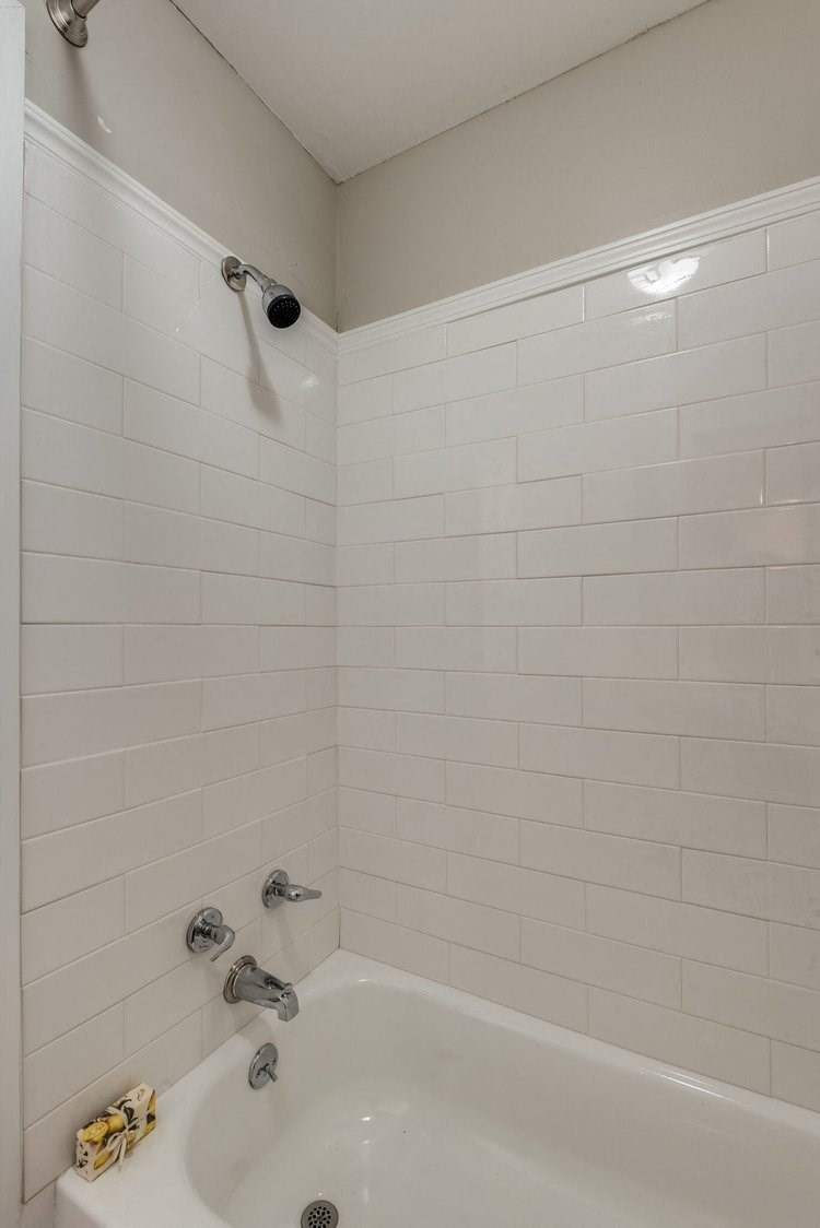 a bathroom with a white tub and a white tiled wall