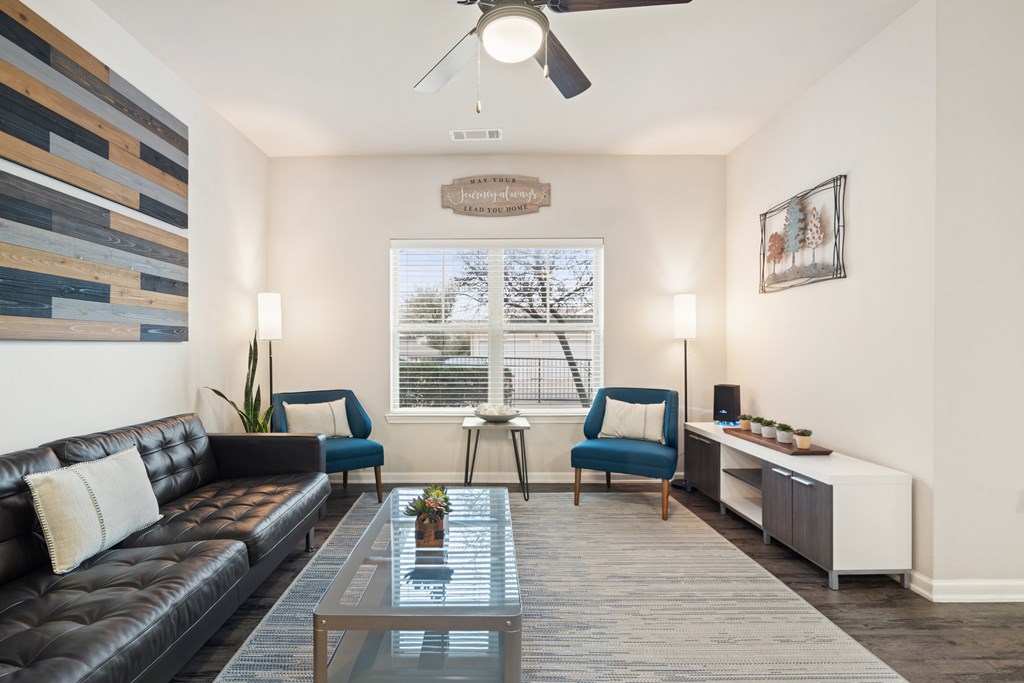 A living room with a black leather couch, a glass coffee table, and a ceiling fan.