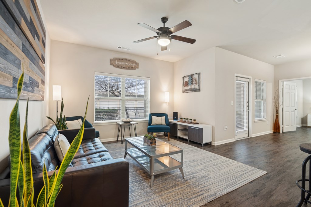 A living room with a brown leather couch, a glass coffee table, and a ceiling fan.