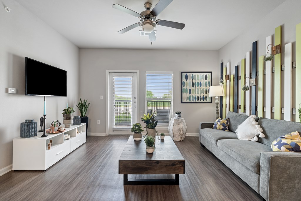 A living room with a grey couch, a wooden coffee table, a flat screen TV, and a ceiling fan.