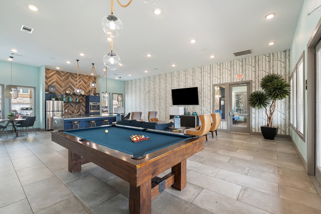 A pool table is in the middle of a room with a tv and a plant.