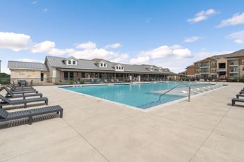 A large swimming pool with lounge chairs and a building in the background.