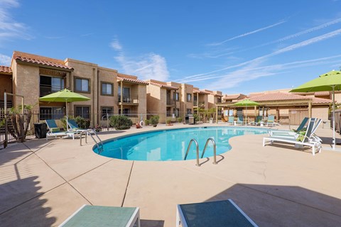A swimming pool surrounded by lounge chairs and umbrellas in a sunny day.