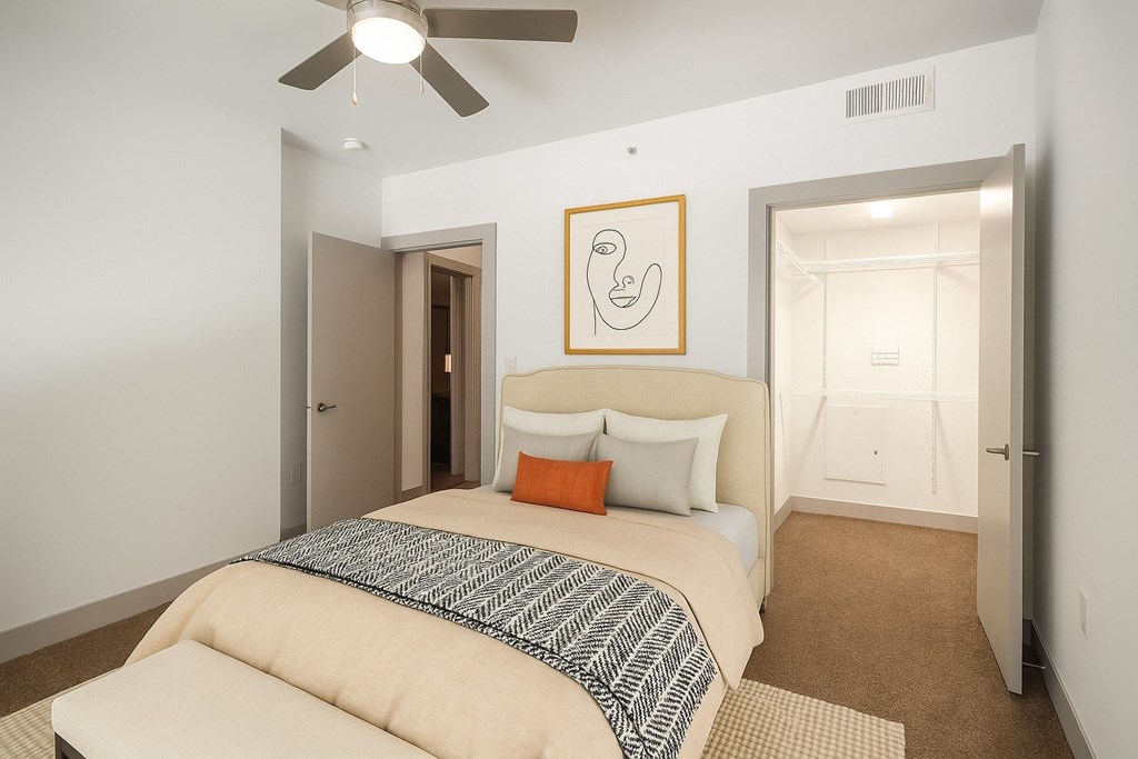 A bedroom with a bed, a ceiling fan, and a painting on the wall.
