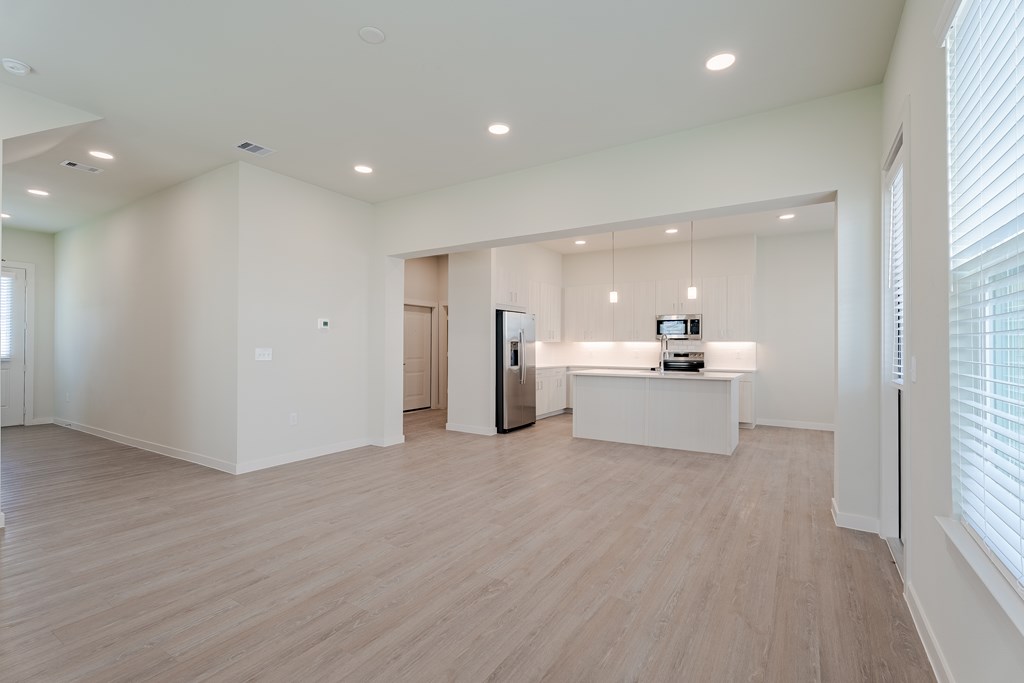 A spacious room with light wood flooring and white walls.