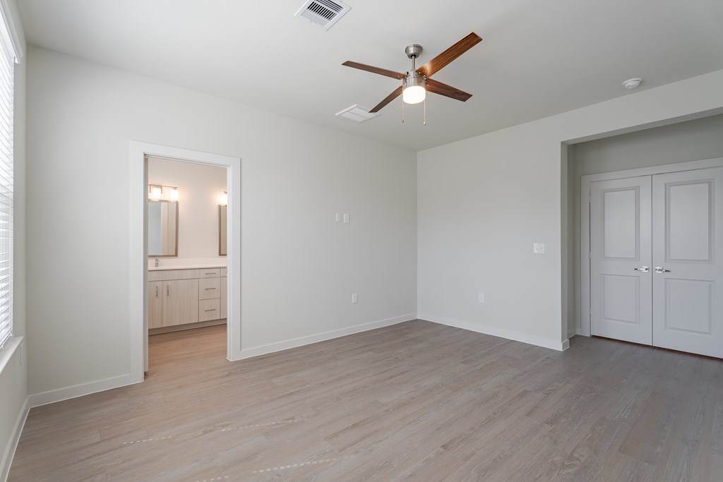 A room with a ceiling fan and light, wooden floors, and white walls.