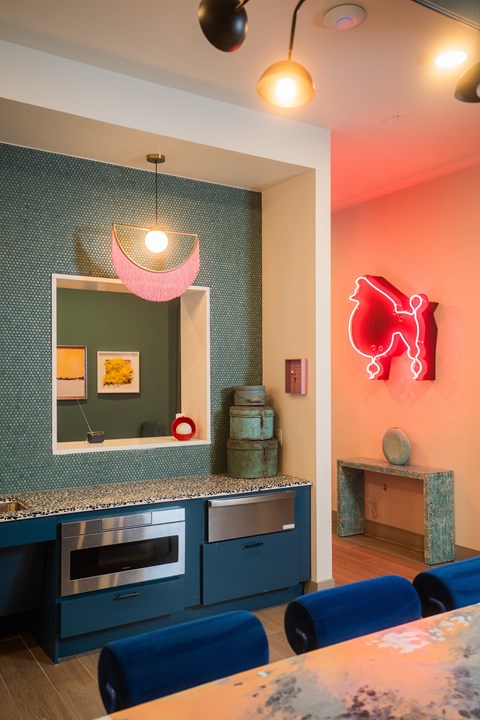 A modern kitchen with blue chairs and a red neon sign on the wall.