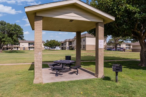 A picnic table is under a pavilion in a grassy area.