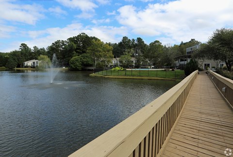 A wooden walkway leads to a fountain in the middle of a lake.