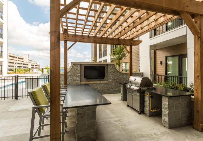 an outdoor kitchen with a grill and a flat screen tv under a wooden pergola