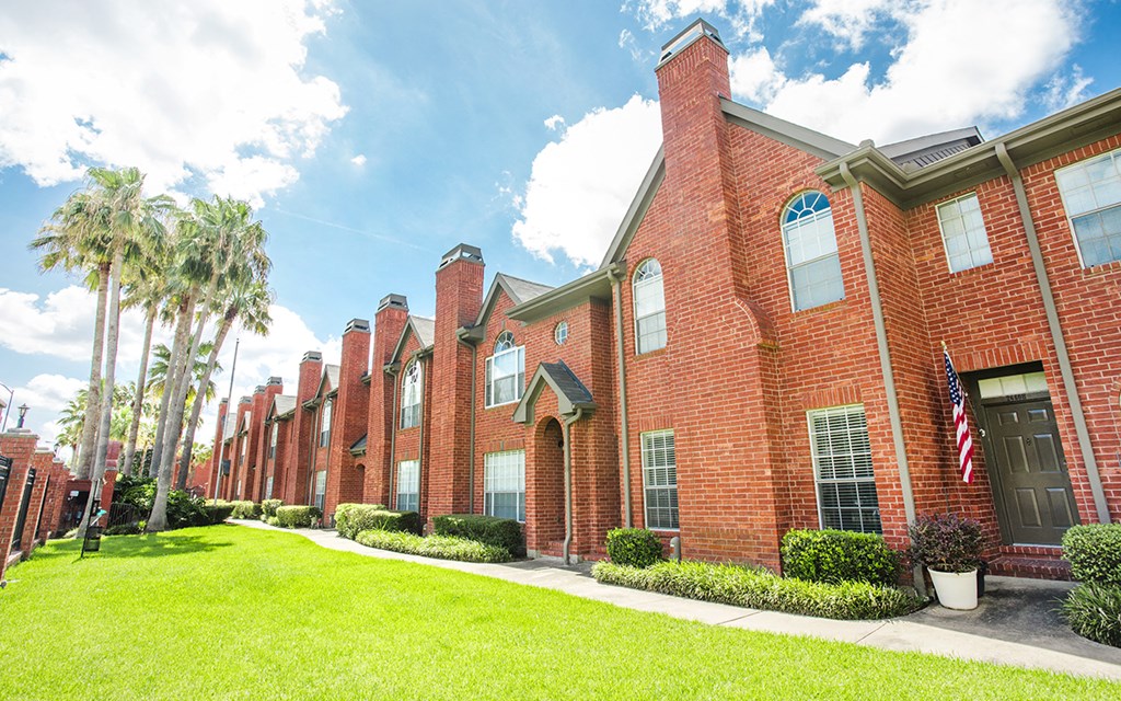 a brick building with a green lawn and palm trees