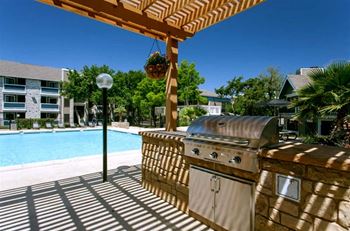 an outdoor kitchen with a grill and a pool in the background